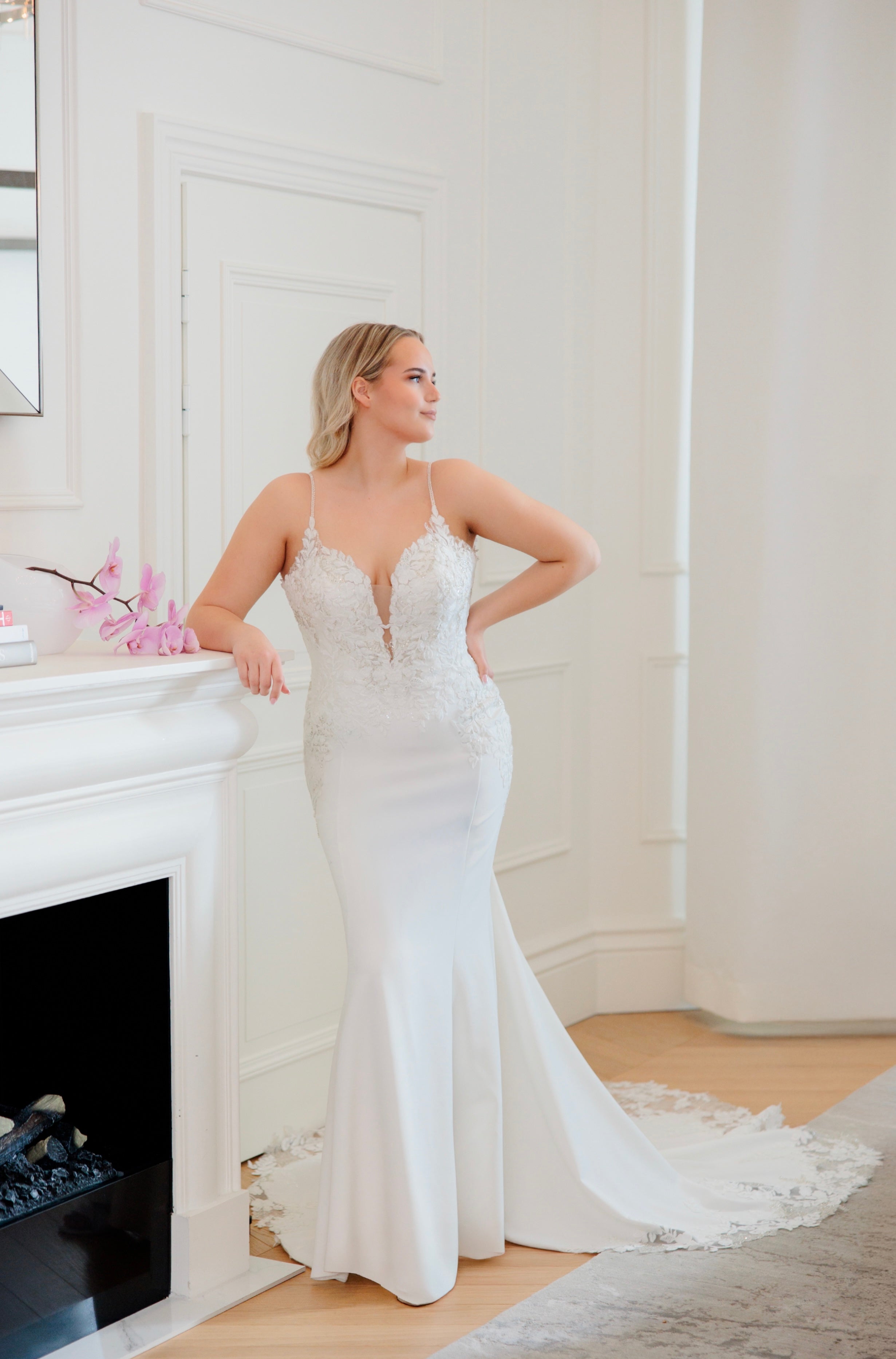 Tyköistuva häämekko ohutolkaisilla, pitsiyksityiskohdilla ja näyttävällä laahuksella, edestä.