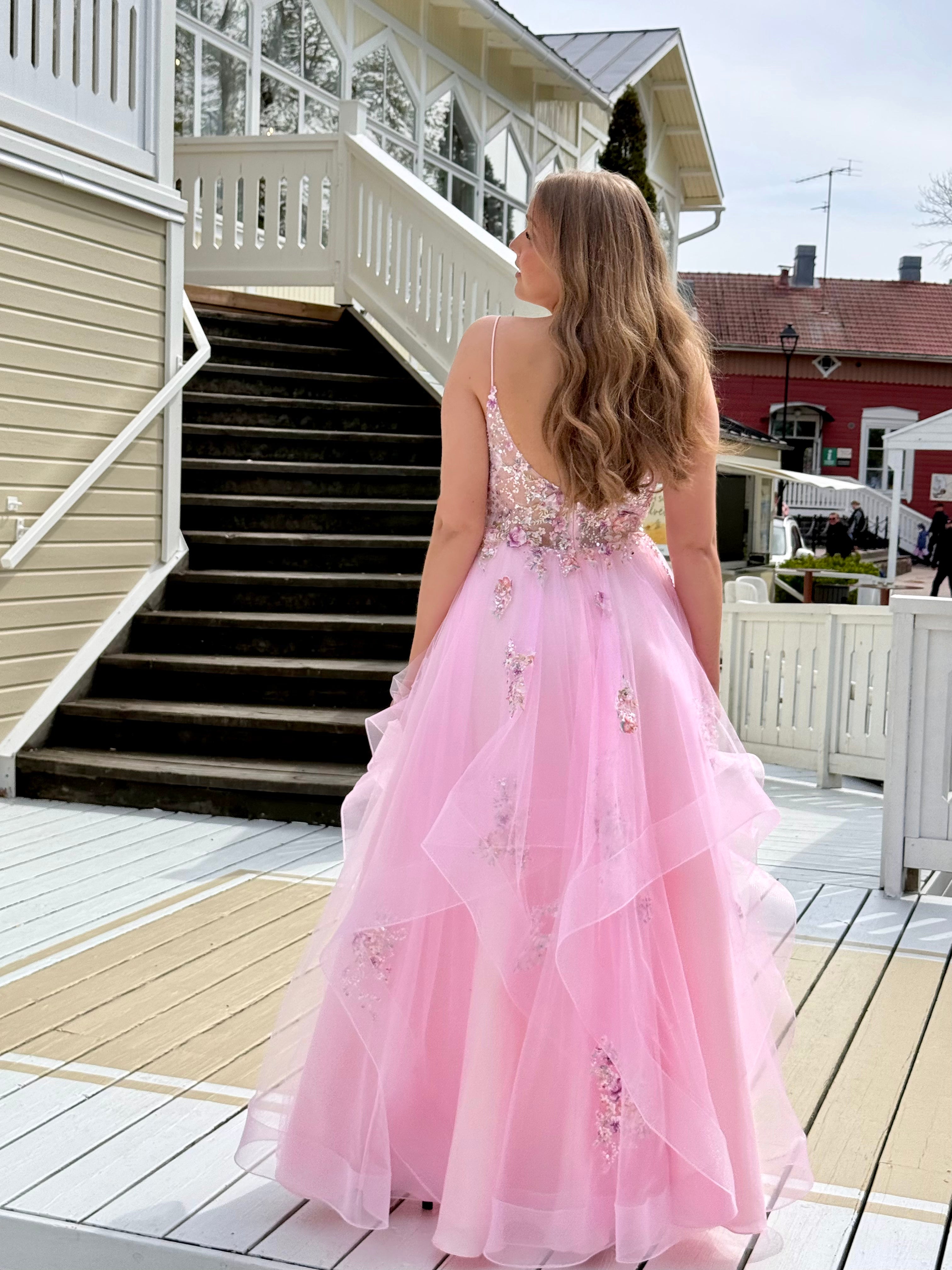 Vaaleanpunainen vanhojentanssimekko kukkapitsillä ja röyhelöhelmalla, takaa.