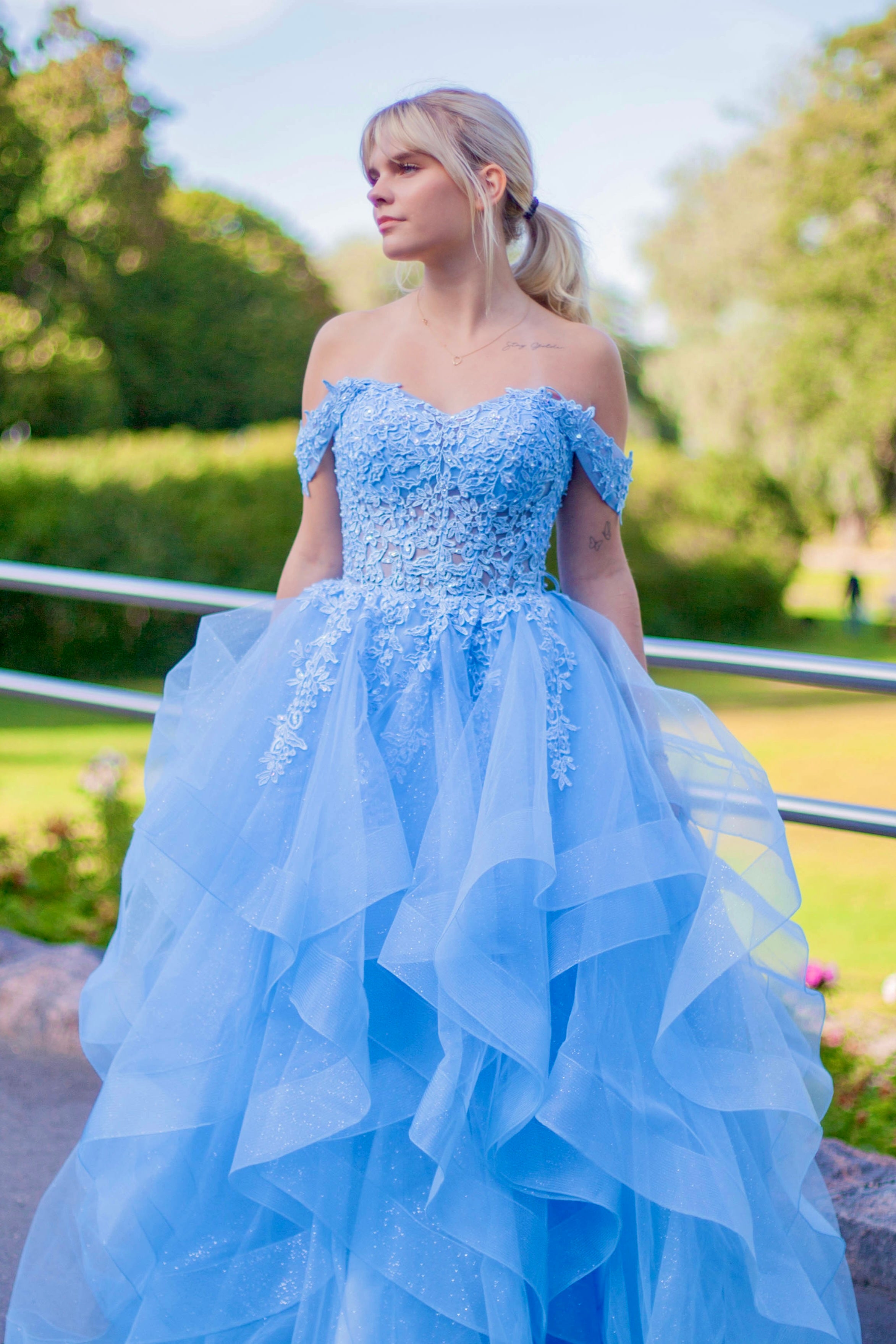 Tämä upea sky blue -sävyinen vanhojentanssimekko hurmaa elegantilla off shoulder -yläosalla, kauniilla pitsiyksityiskohdilla ja näyttävällä röyhelöhelmalla.