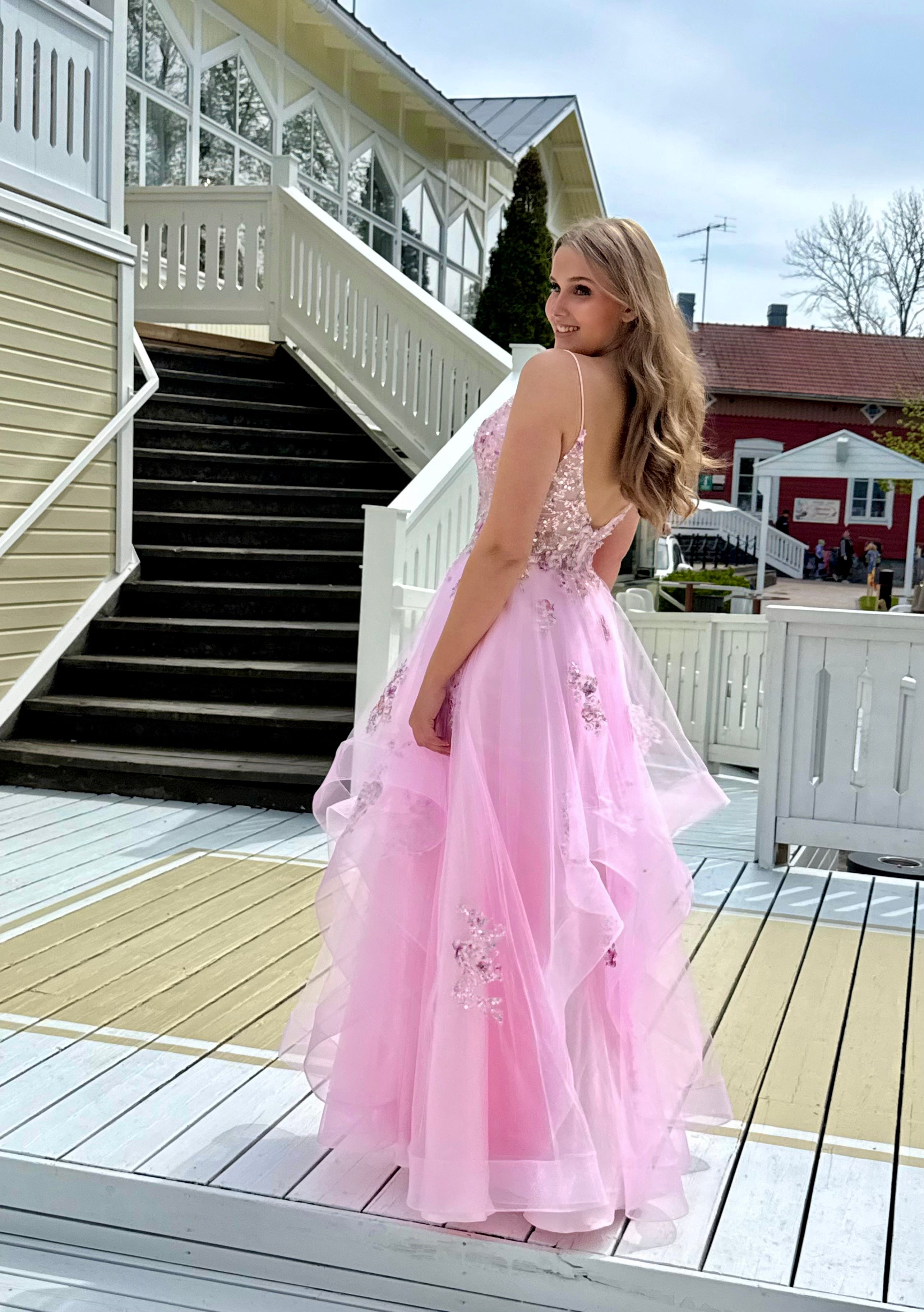 Vaaleanpunainen vanhojentanssimekko kukkapitsillä ja röyhelöhelmalla, takaa.