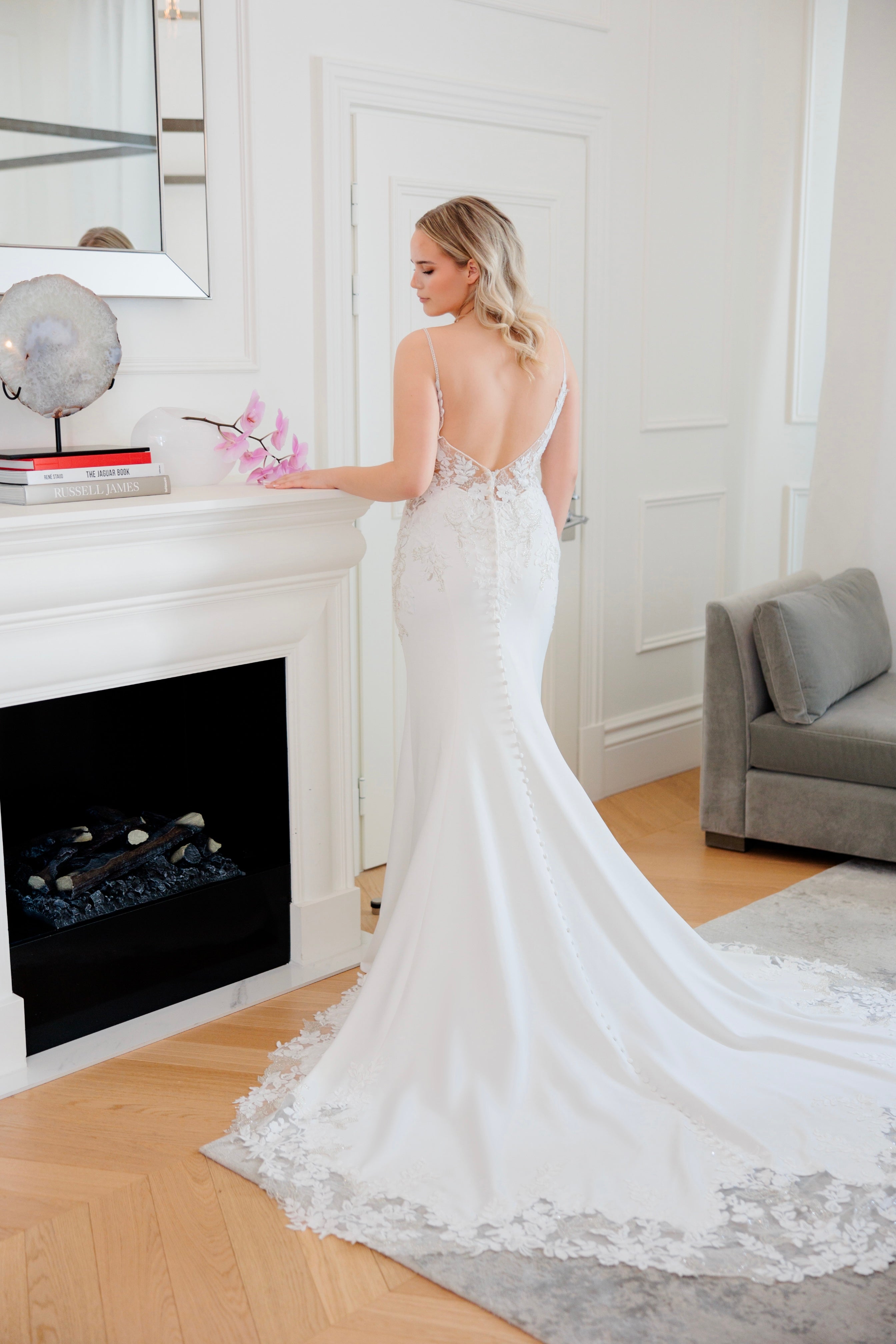 Tyköistuva häämekko ohutolkaisilla, pitsiyksityiskohdilla ja näyttävällä laahuksella.