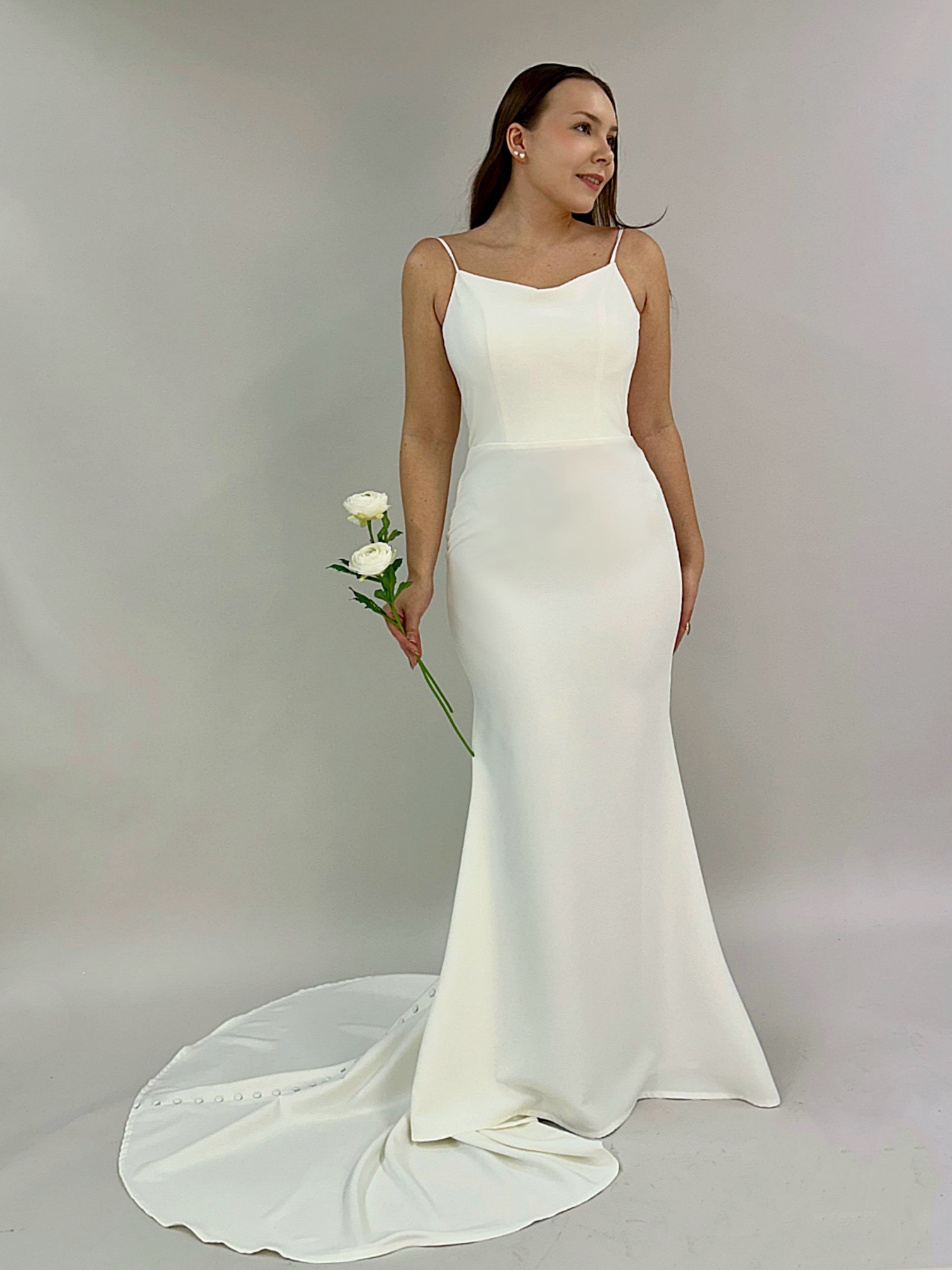 Minimalistinen häämekko ohuilla olkaimilla, syvään uurrettu V-selkä ja napitus selästä laahukseen.