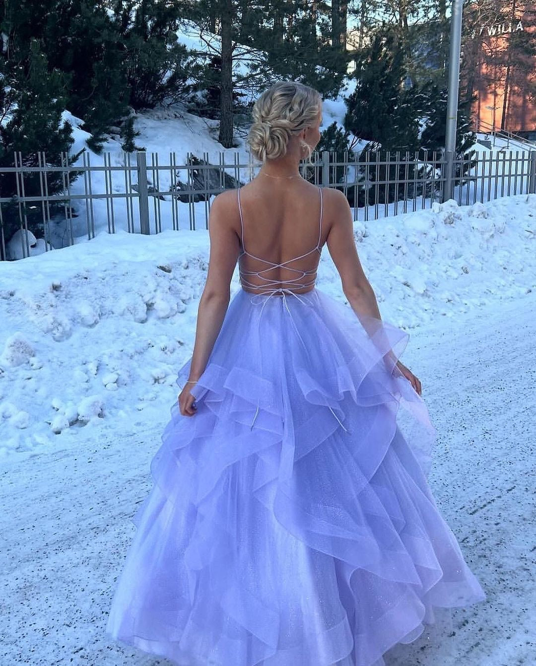 Violetti vanhojentanssimekko kimaltavalla röyhelöhelmalla ja avoimella selällä, takaa.