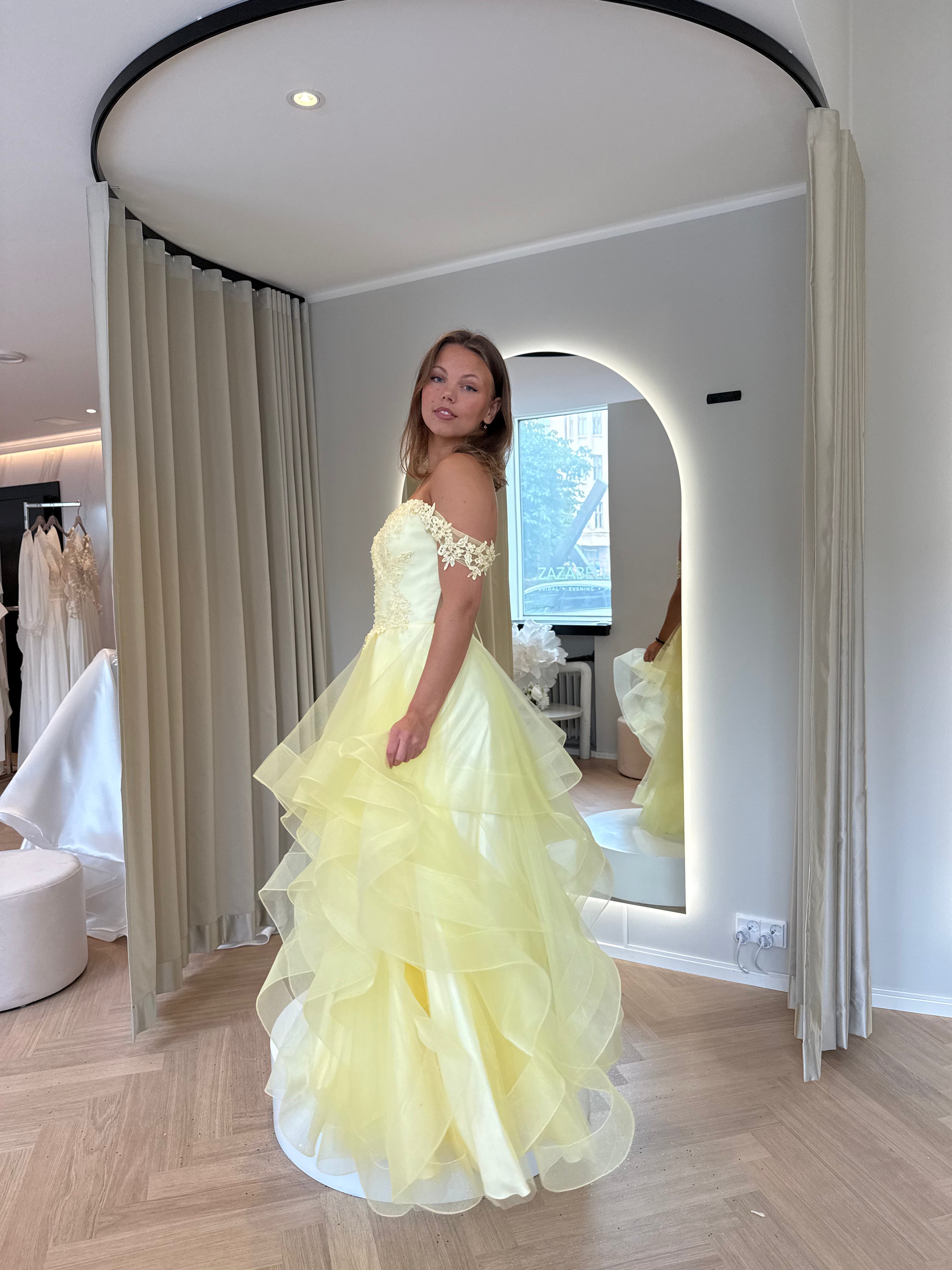 Keltainen vanhojentanssimekko off shoulder -mallisella pitsiyläosalla ja röyhelöhelmalla.