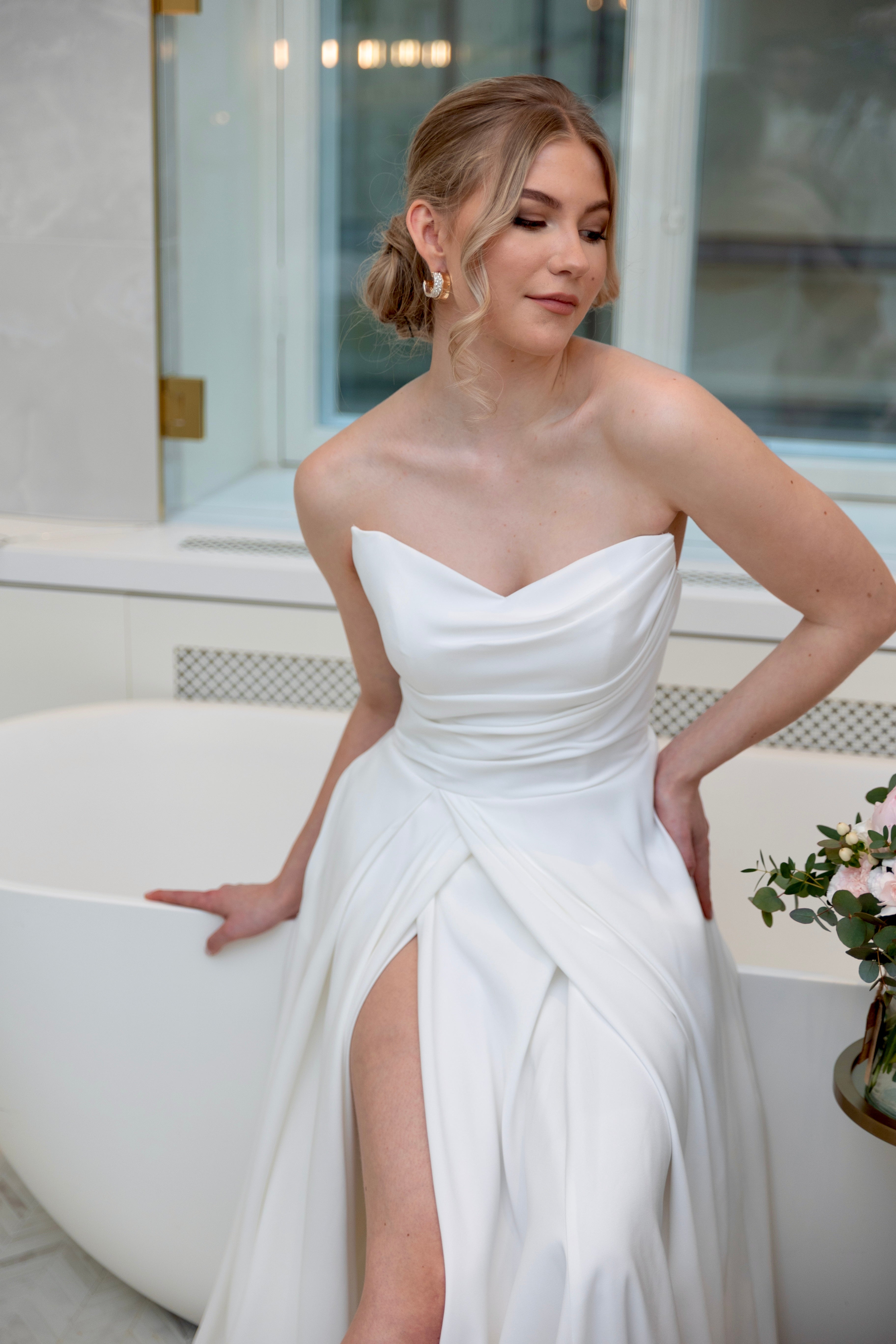 Häämekko laskeutuvalla materiaalilla ja rypytyksellä, klassinen siluetti ja moderni tyyli.