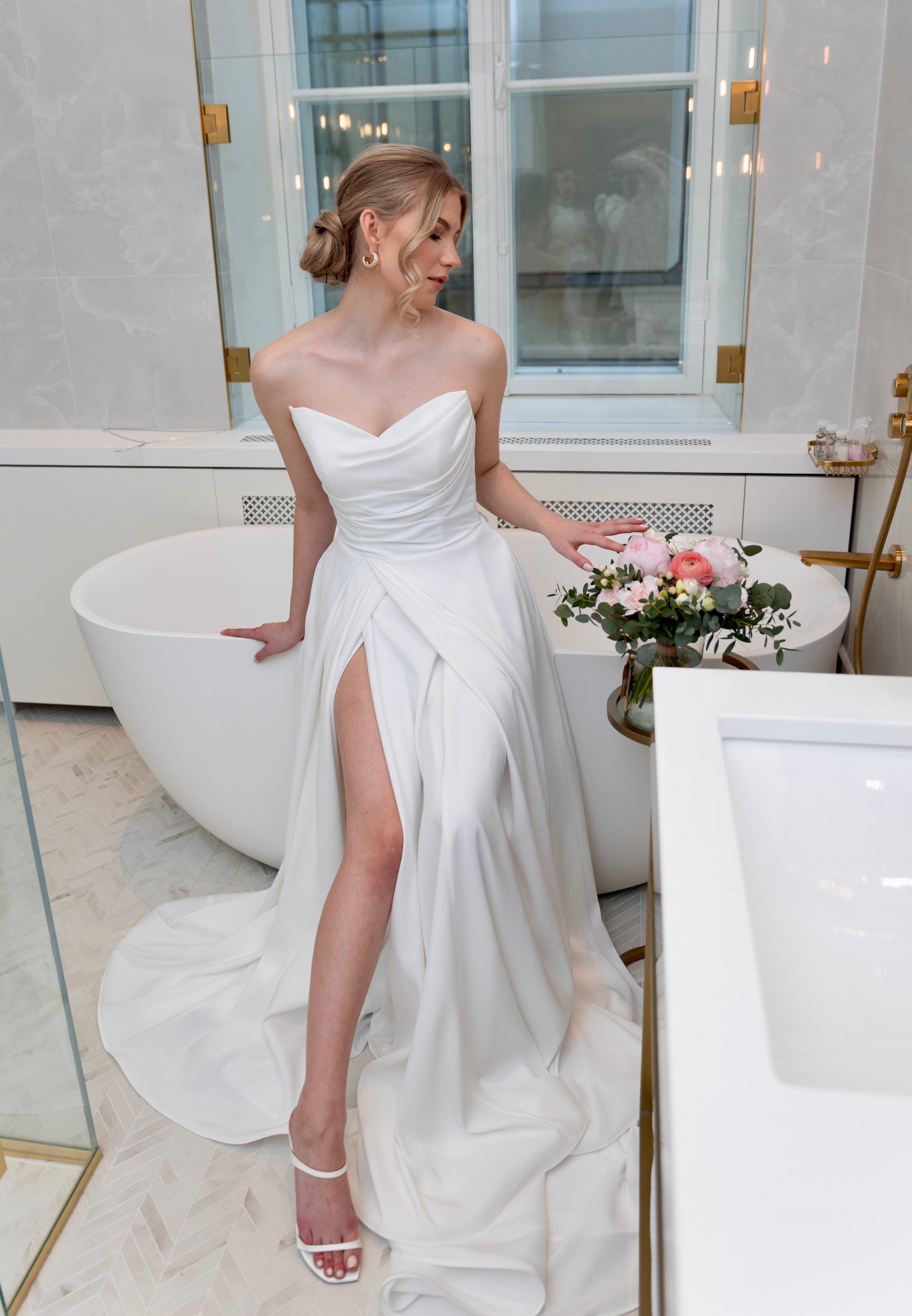 Häämekko laskeutuvalla materiaalilla ja rypytyksellä, klassinen siluetti ja moderni tyyli.