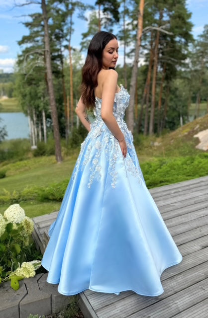 Vaaleansininen satiininen vanhojentanssimekko olkaimettomalla mallilla, koristeltu kukkapitsillä, sivulta.