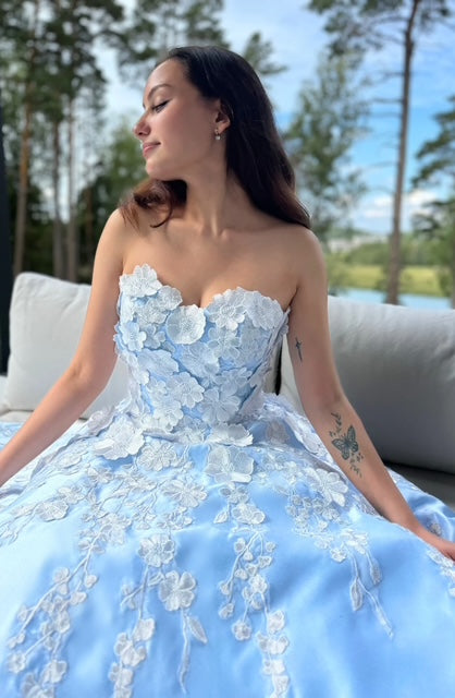 Vaaleansininen satiininen vanhojentanssimekko olkaimettomalla mallilla, koristeltu kukkapitsillä, edestä.