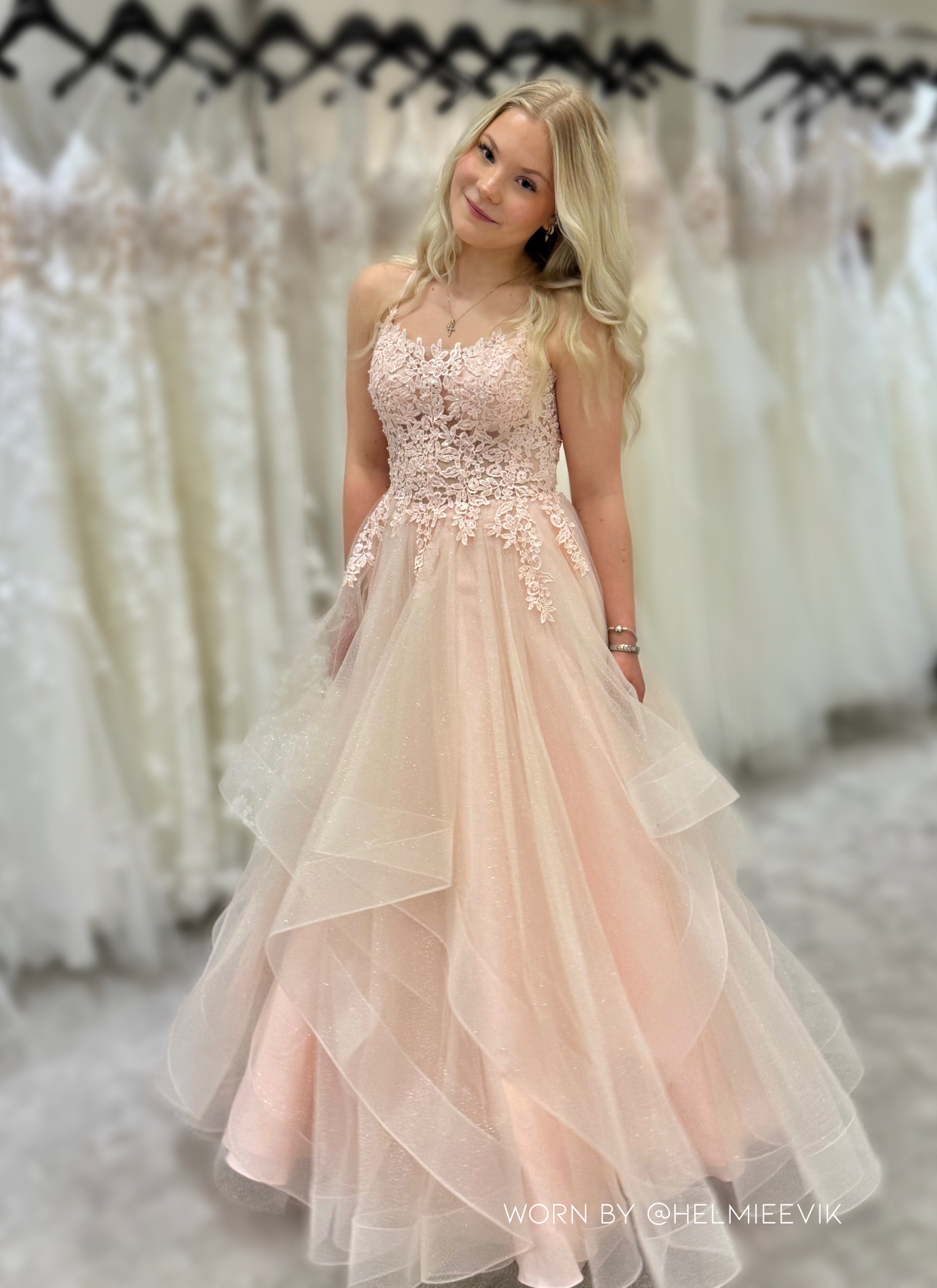 Vaaleanpunainen vanhojentanssimekko, röyhelöhelma, kimallus ja pitsikoristeinen yläosa.