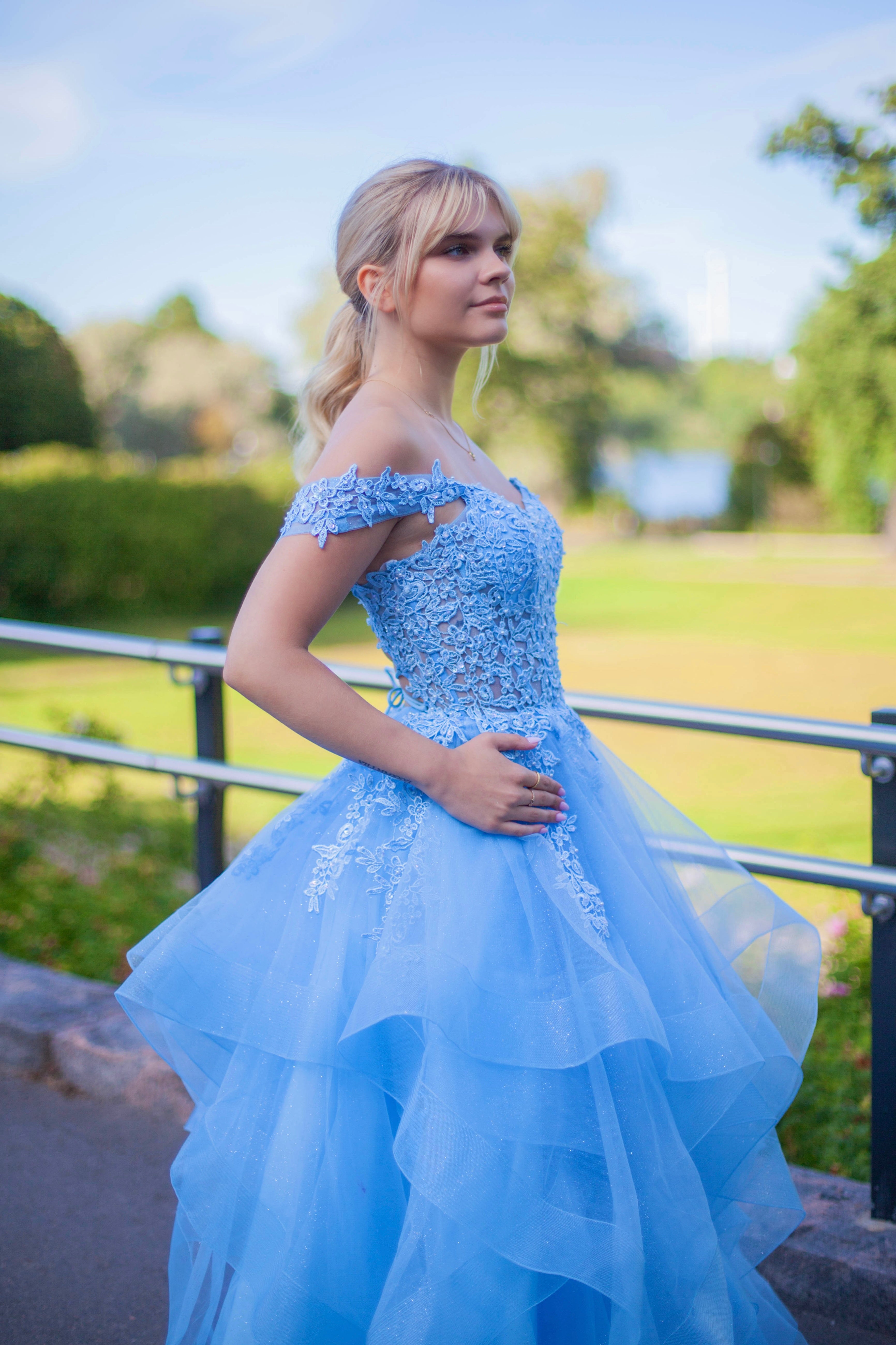 Tämä upea sky blue -sävyinen vanhojentanssimekko hurmaa elegantilla off shoulder -yläosalla, kauniilla pitsiyksityiskohdilla ja näyttävällä röyhelöhelmalla.