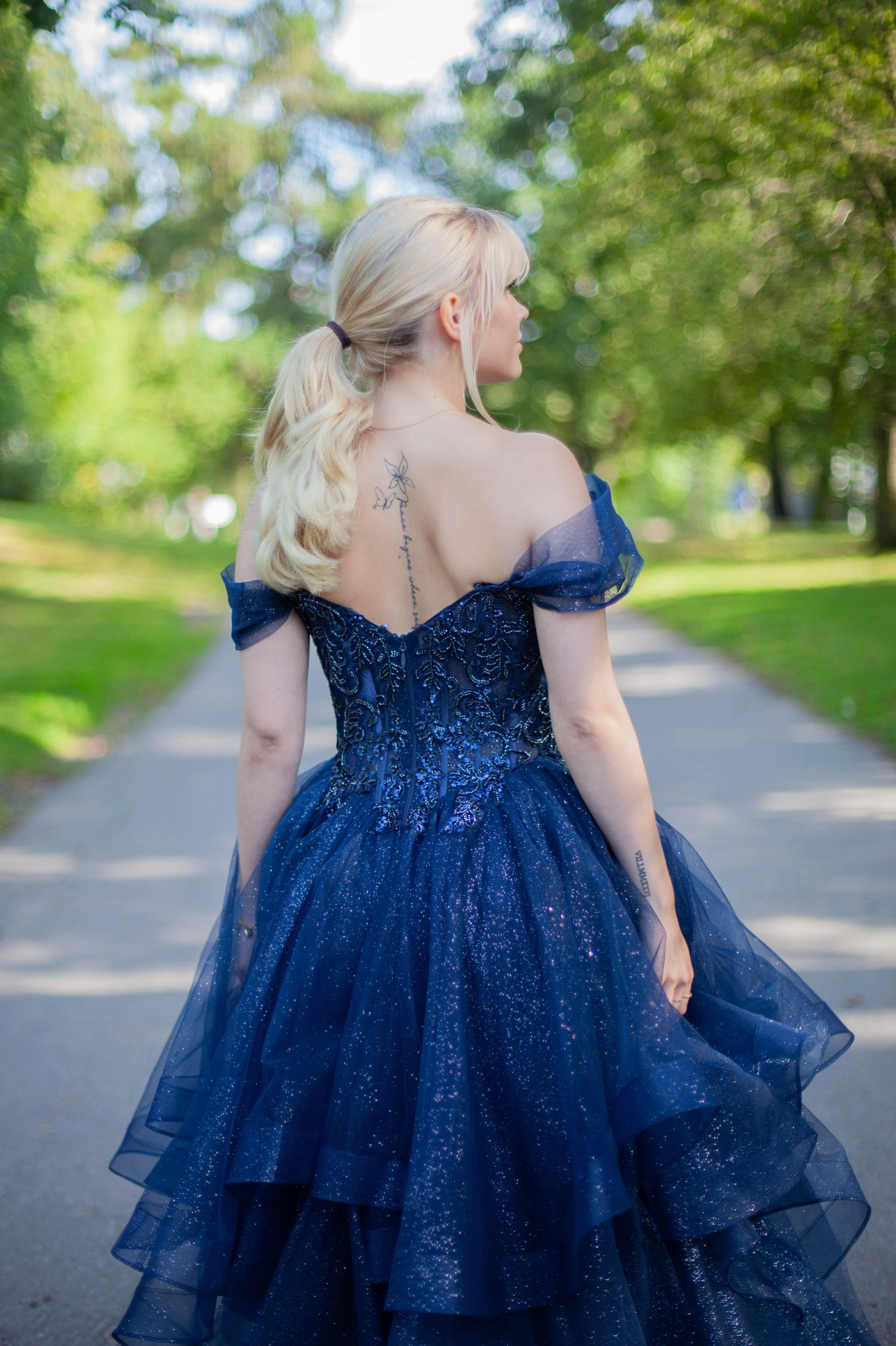 Kimaltava tummansininen vanhojentanssimekko off shoulder -yläosalla ja näyttävällä röyhelöhelmalla.