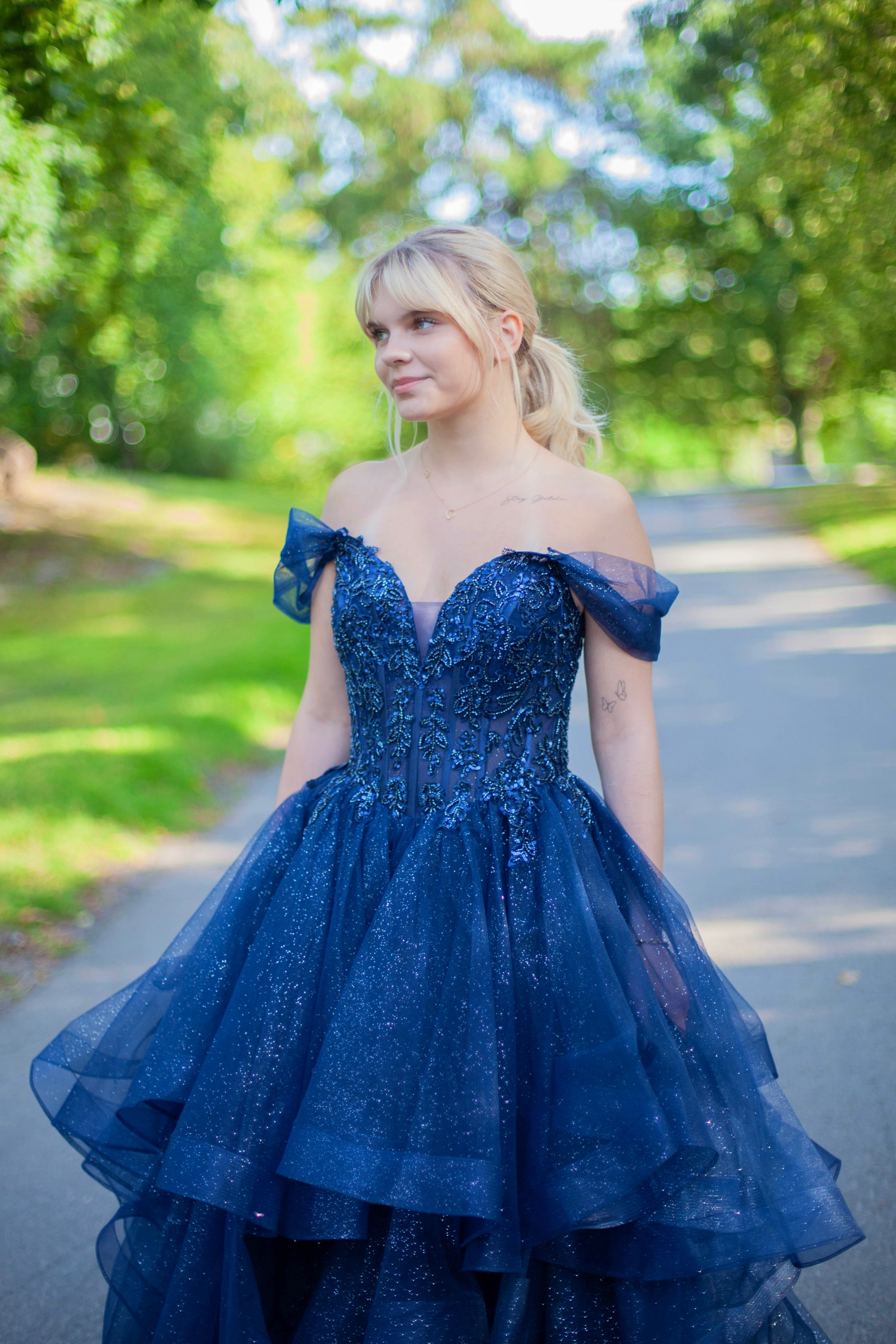 Kimaltava tummansininen vanhojentanssimekko off shoulder -yläosalla ja näyttävällä röyhelöhelmalla.