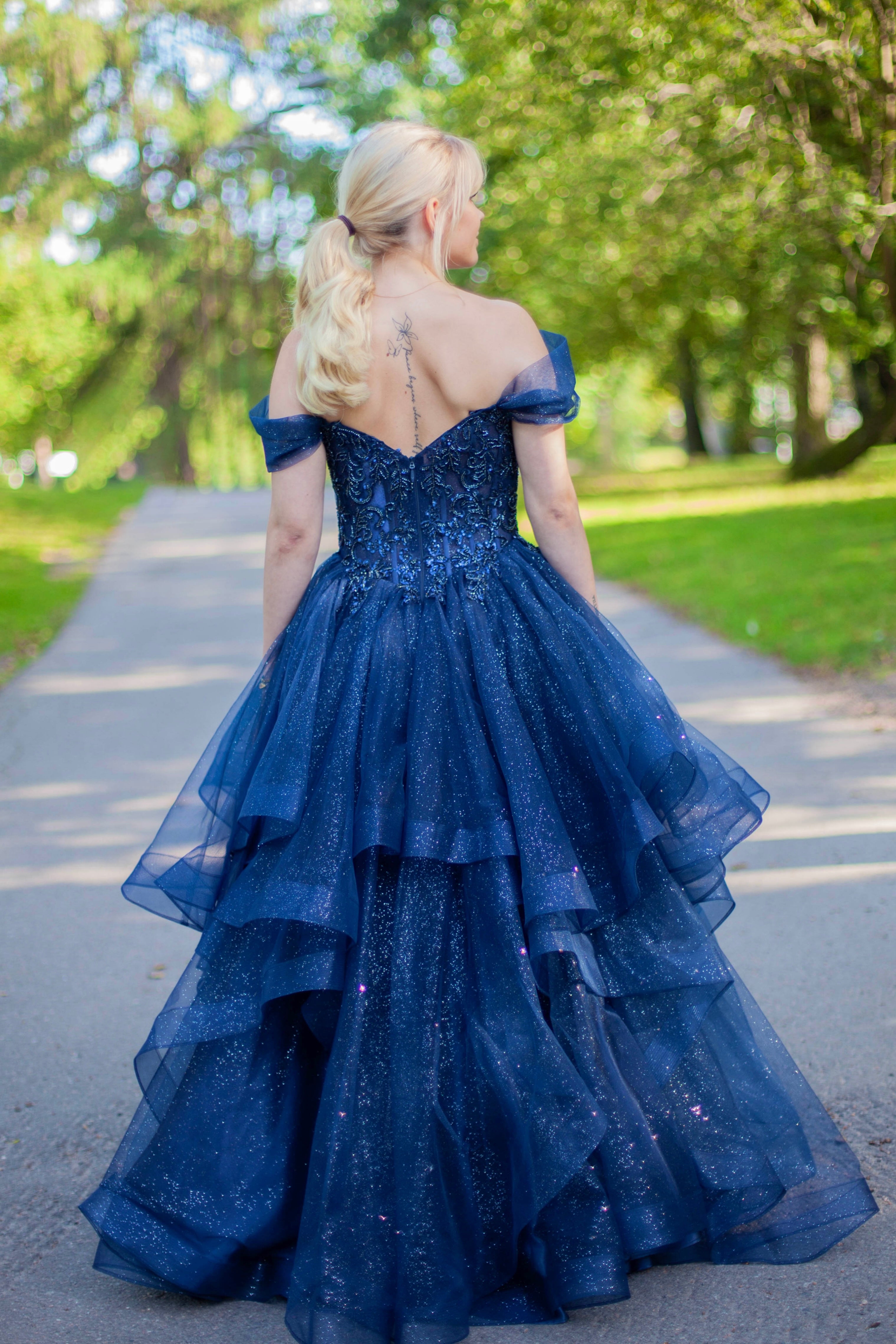 Kimaltava tummansininen vanhojentanssimekko off shoulder -yläosalla ja näyttävällä röyhelöhelmalla.