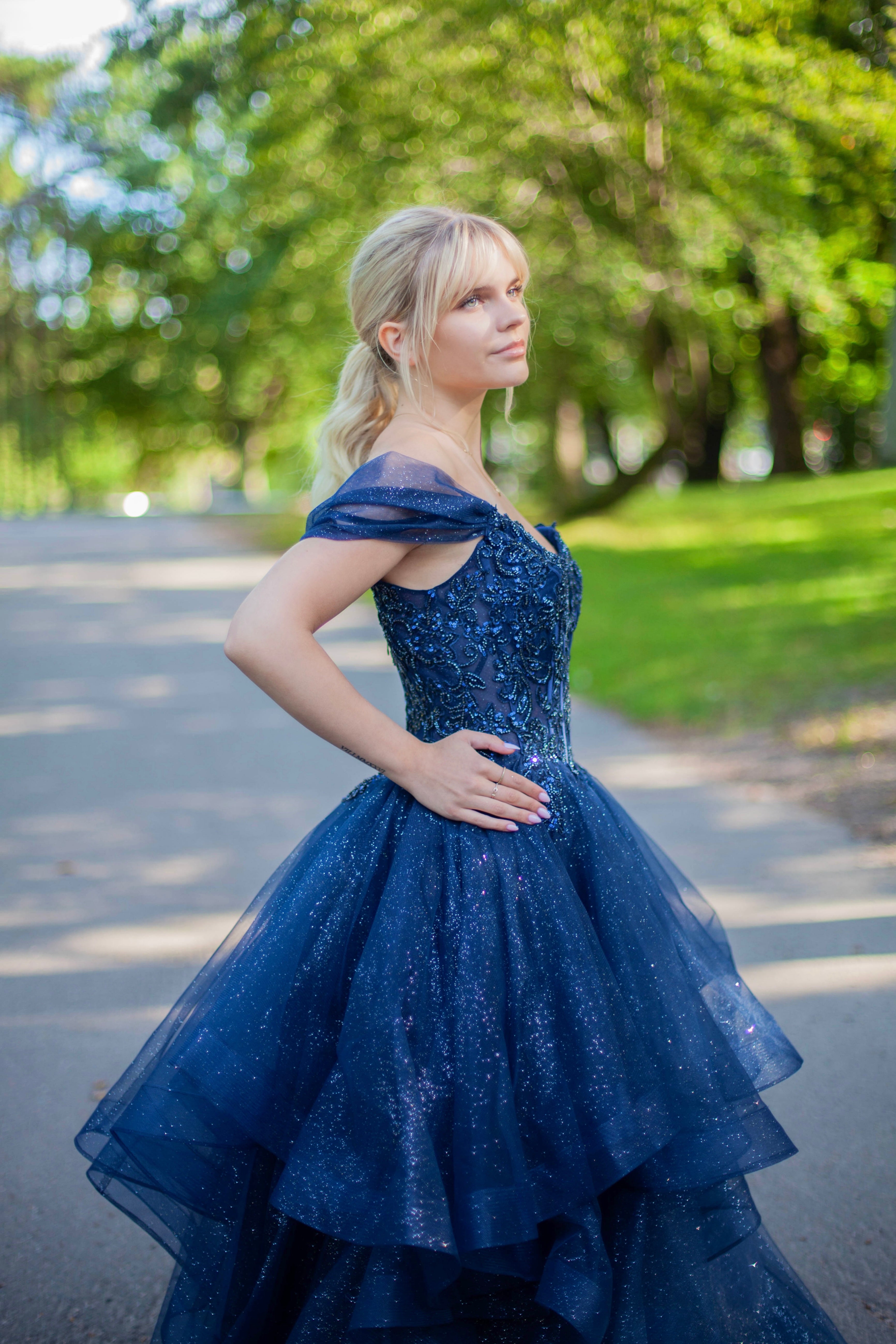 Kimaltava tummansininen vanhojentanssimekko off shoulder -yläosalla ja näyttävällä röyhelöhelmalla.