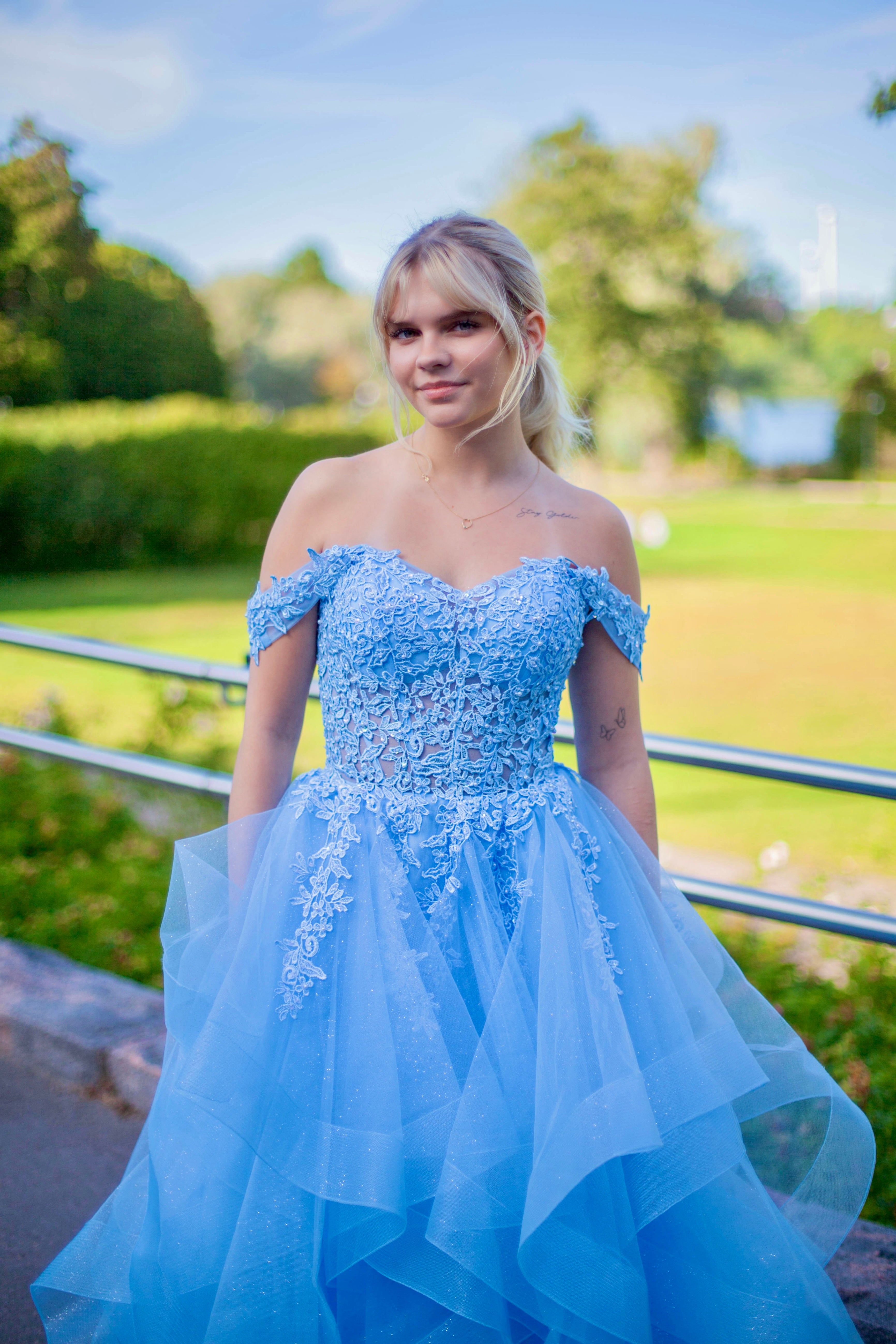 Tämä upea sky blue -sävyinen vanhojentanssimekko hurmaa elegantilla off shoulder -yläosalla, kauniilla pitsiyksityiskohdilla ja näyttävällä röyhelöhelmalla.