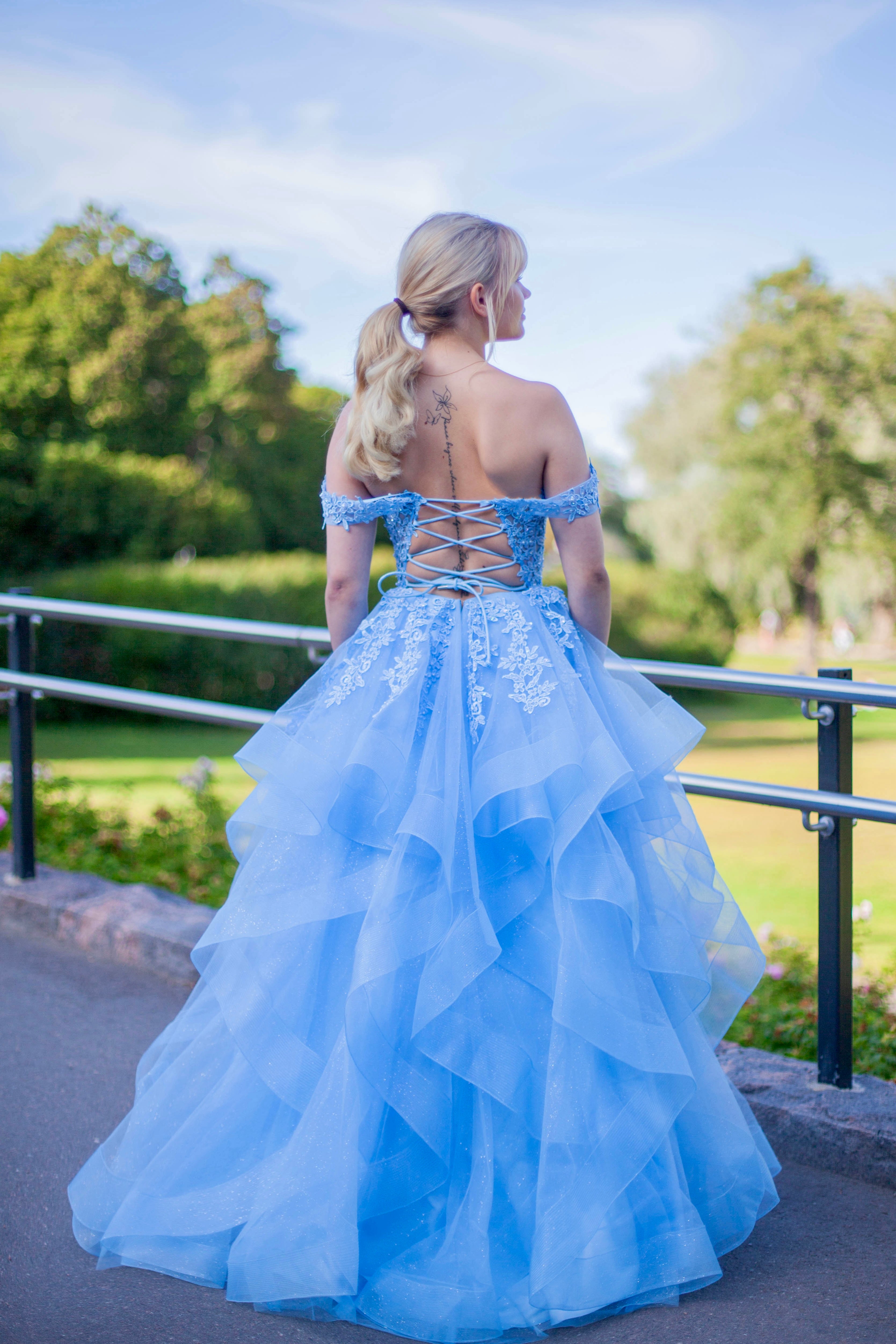 Tämä upea sky blue -sävyinen vanhojentanssimekko hurmaa elegantilla off shoulder -yläosalla, kauniilla pitsiyksityiskohdilla ja näyttävällä röyhelöhelmalla.
