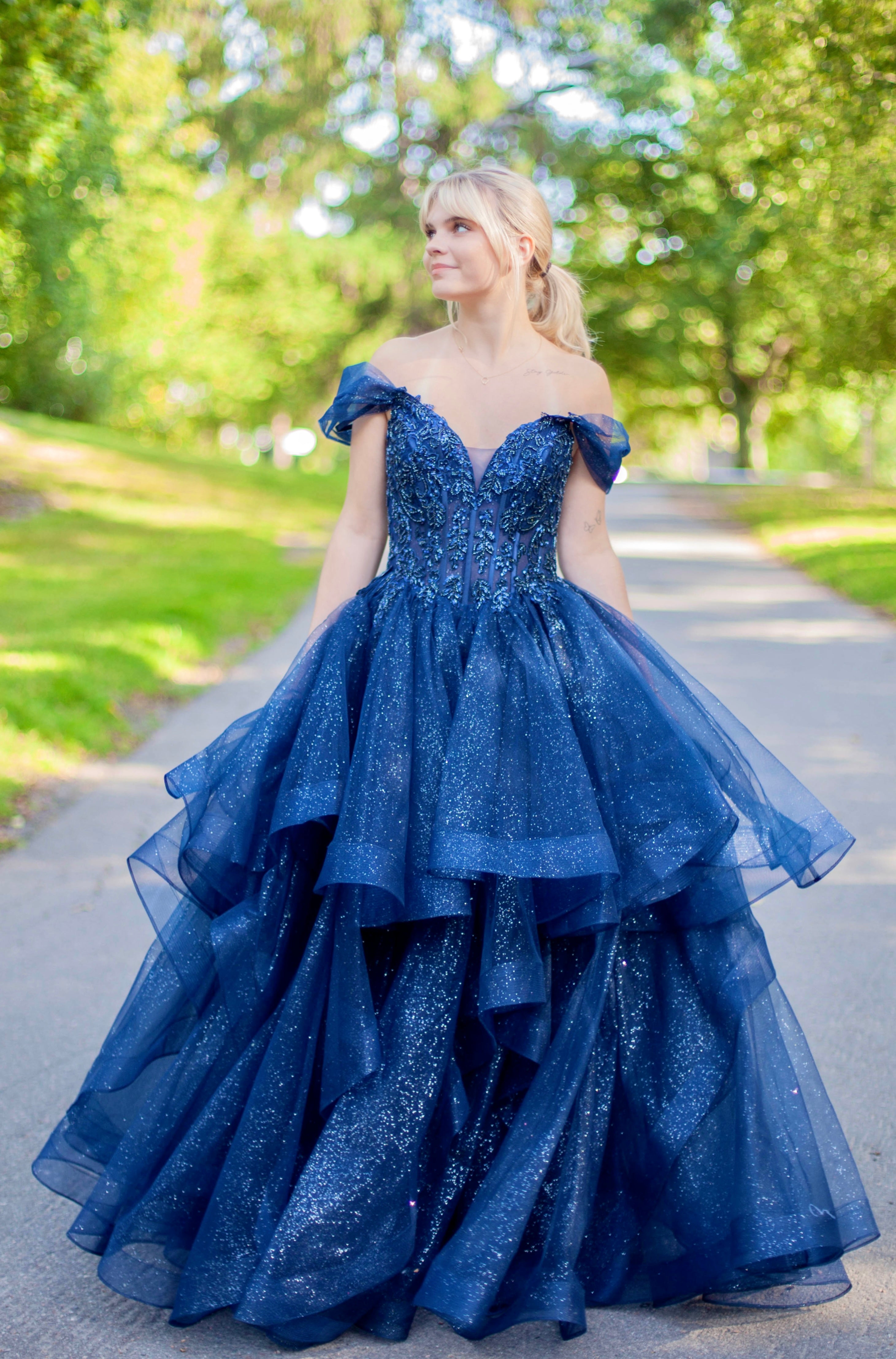 Kimaltava tummansininen vanhojentanssimekko off shoulder -yläosalla ja näyttävällä röyhelöhelmalla.