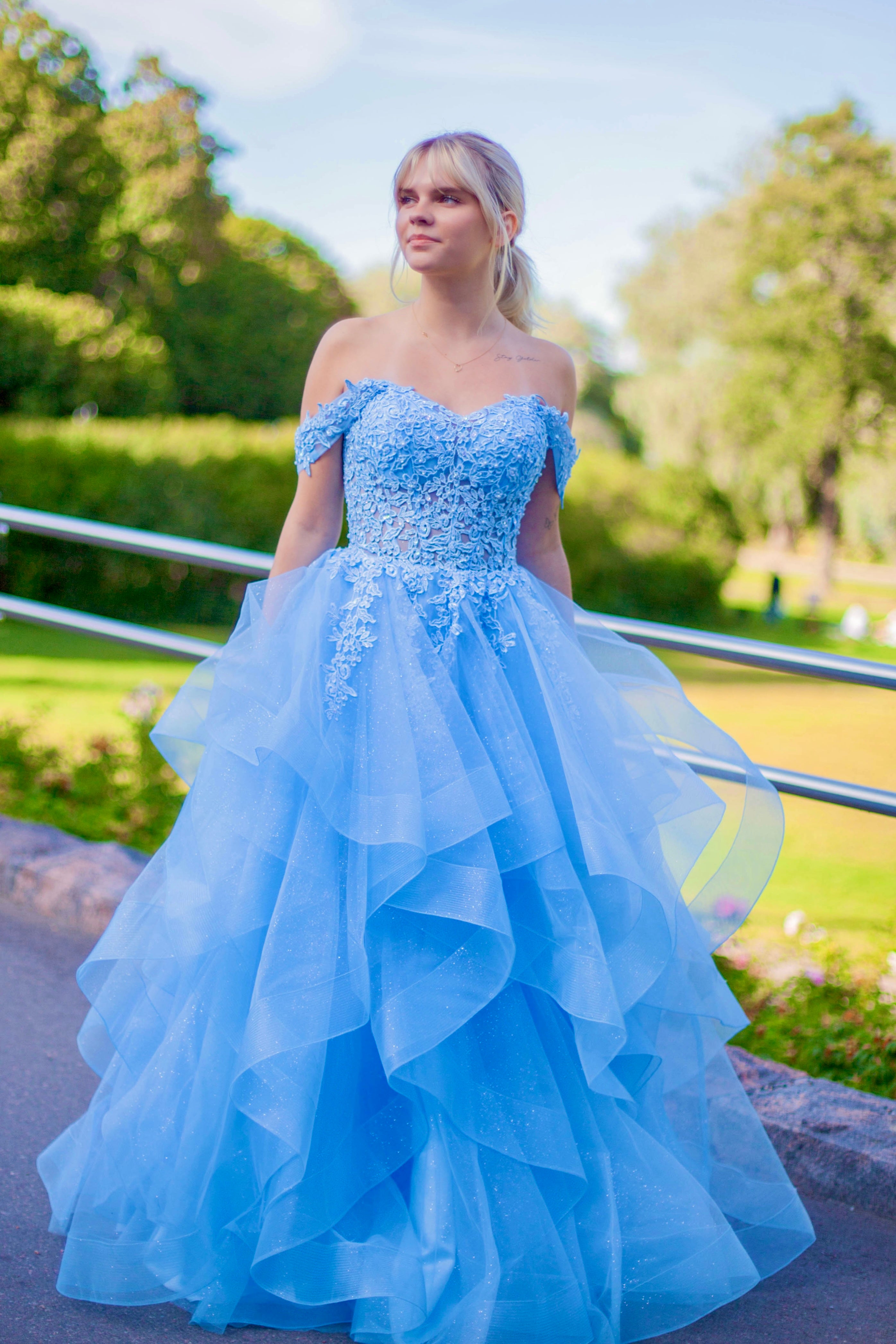 Tämä upea sky blue -sävyinen vanhojentanssimekko hurmaa elegantilla off shoulder -yläosalla, kauniilla pitsiyksityiskohdilla ja näyttävällä röyhelöhelmalla.
