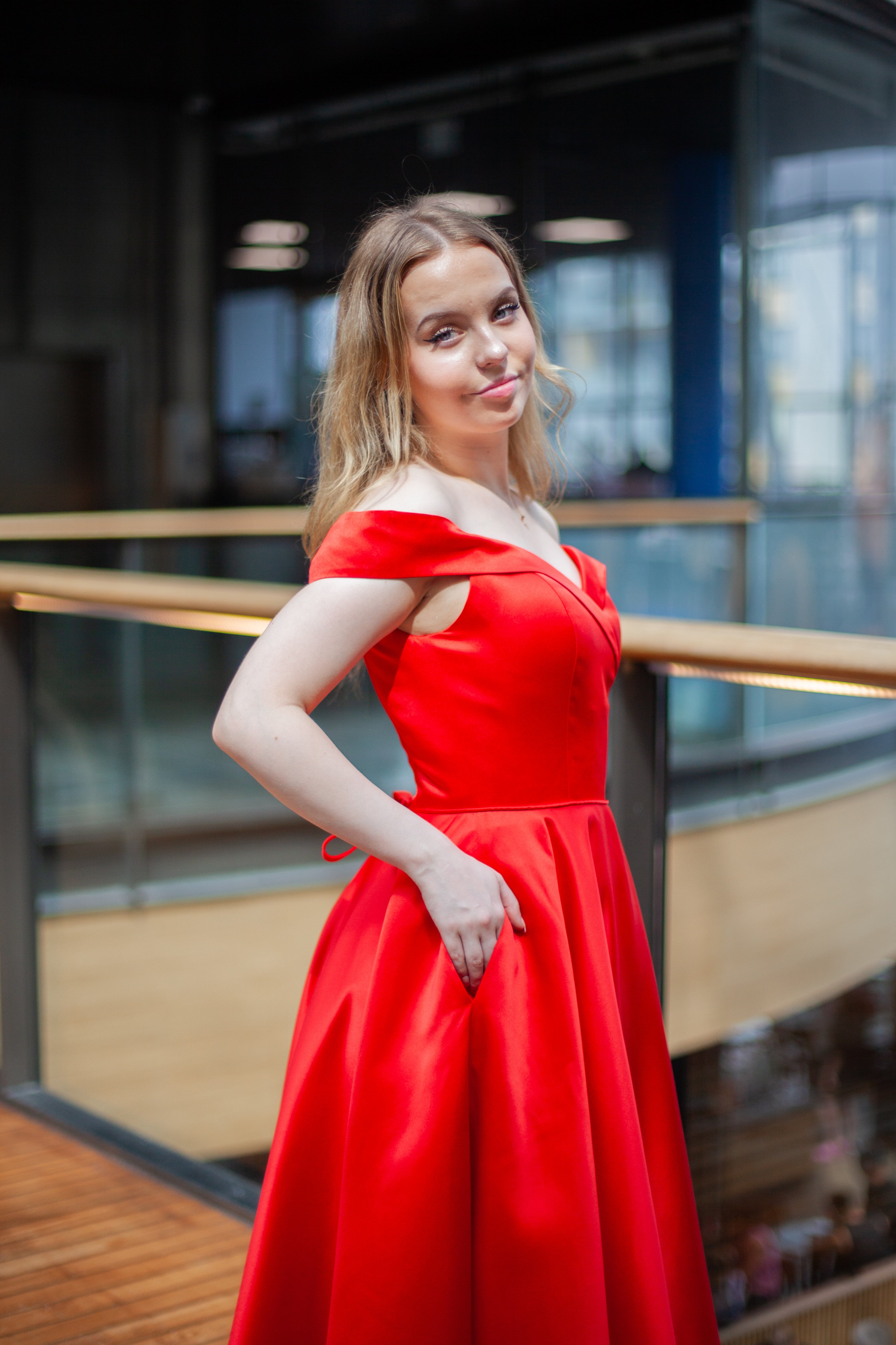 Punainen vanhojentanssimekko off shoulder -olkaimilla ja kauniisti laskeutuvalla helmalla, sivusta.
